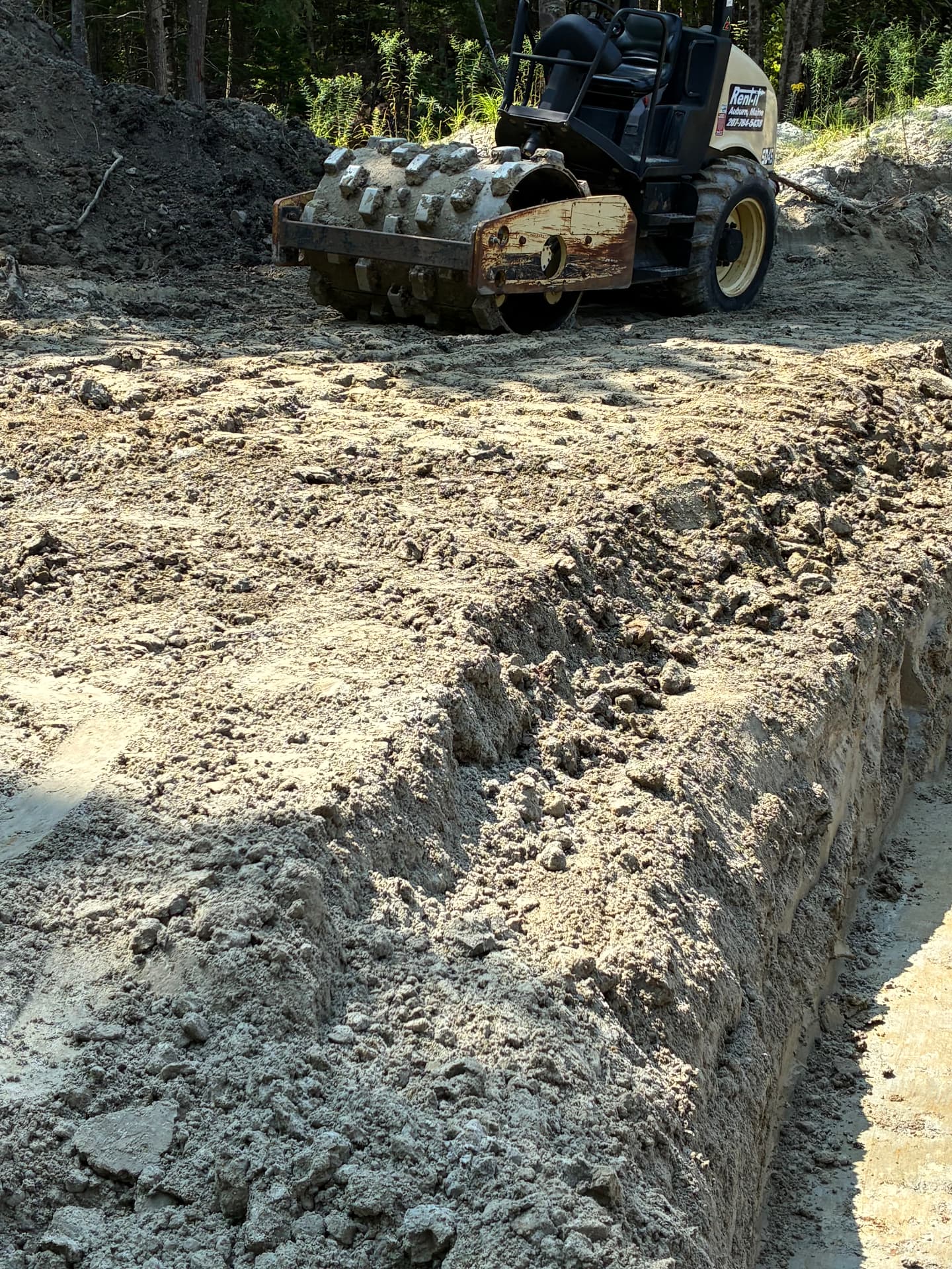 Sheepsfoot roller compacting the pond embankment beside a cut trench