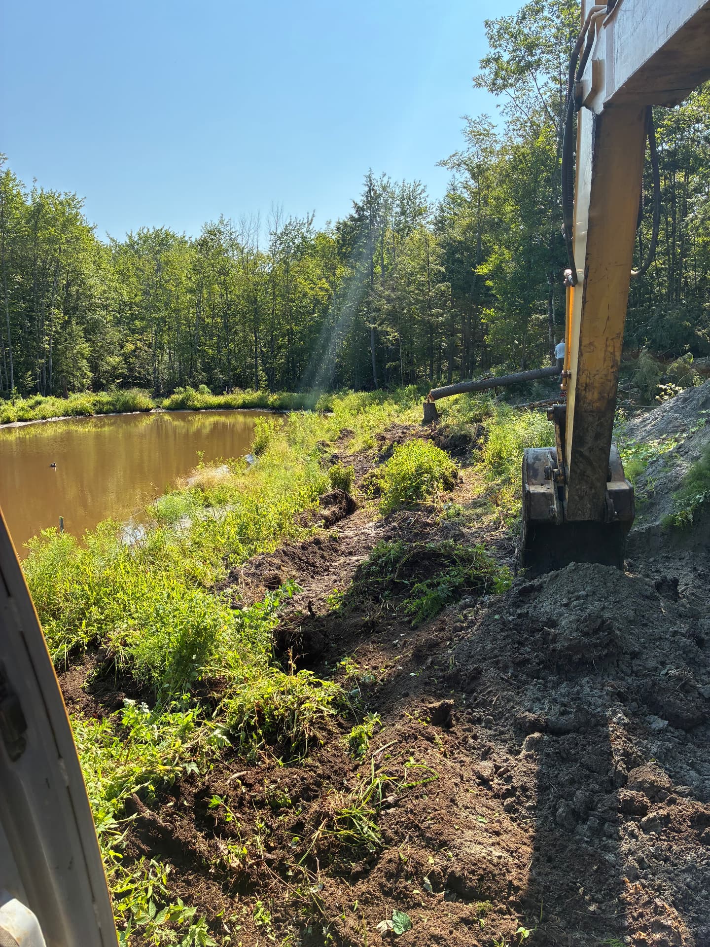 Excavator clearing and shaping the bank along the edge of the pond