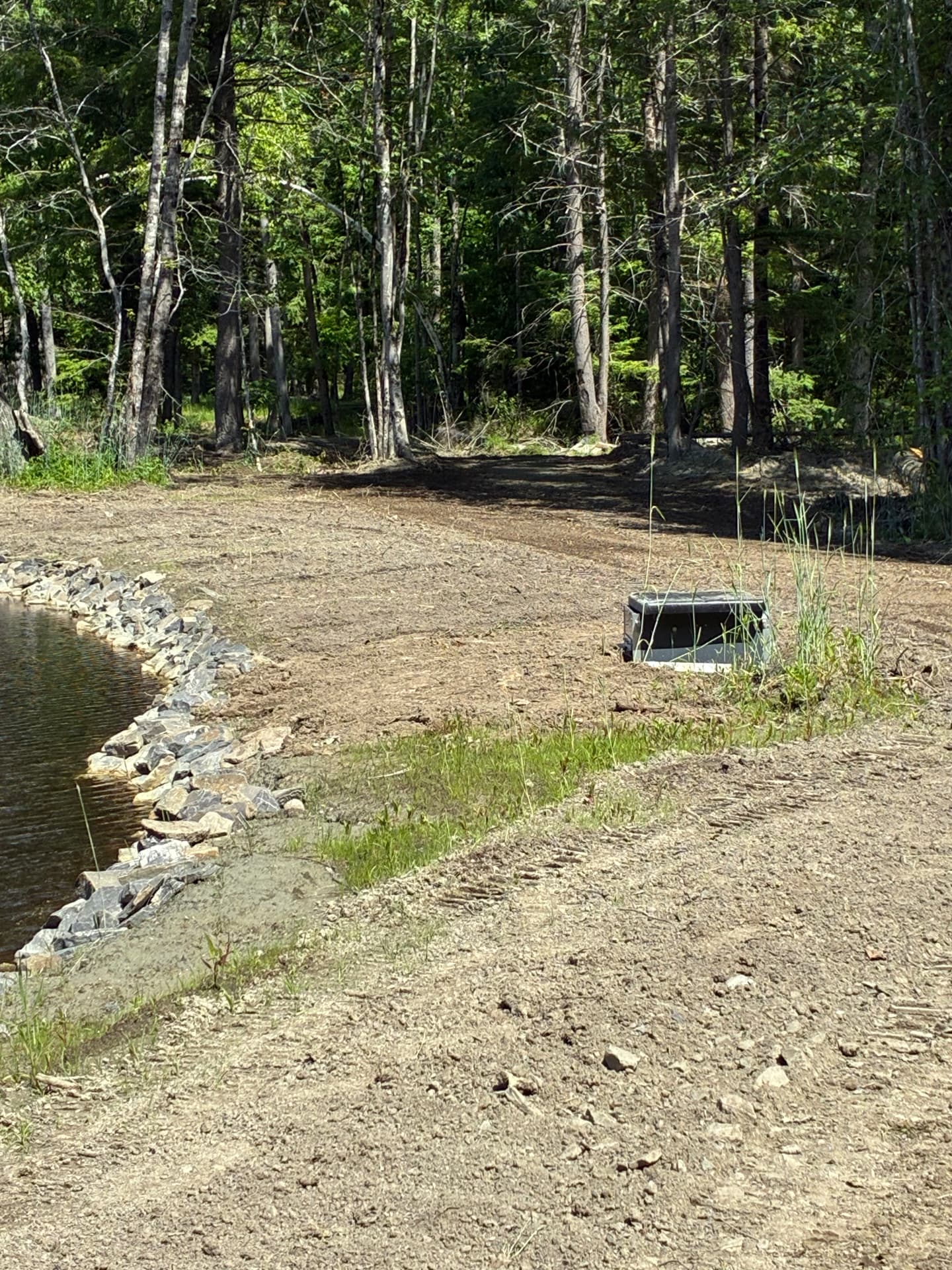 Stone riprap set along a new pond shoreline with the embankment graded behind it