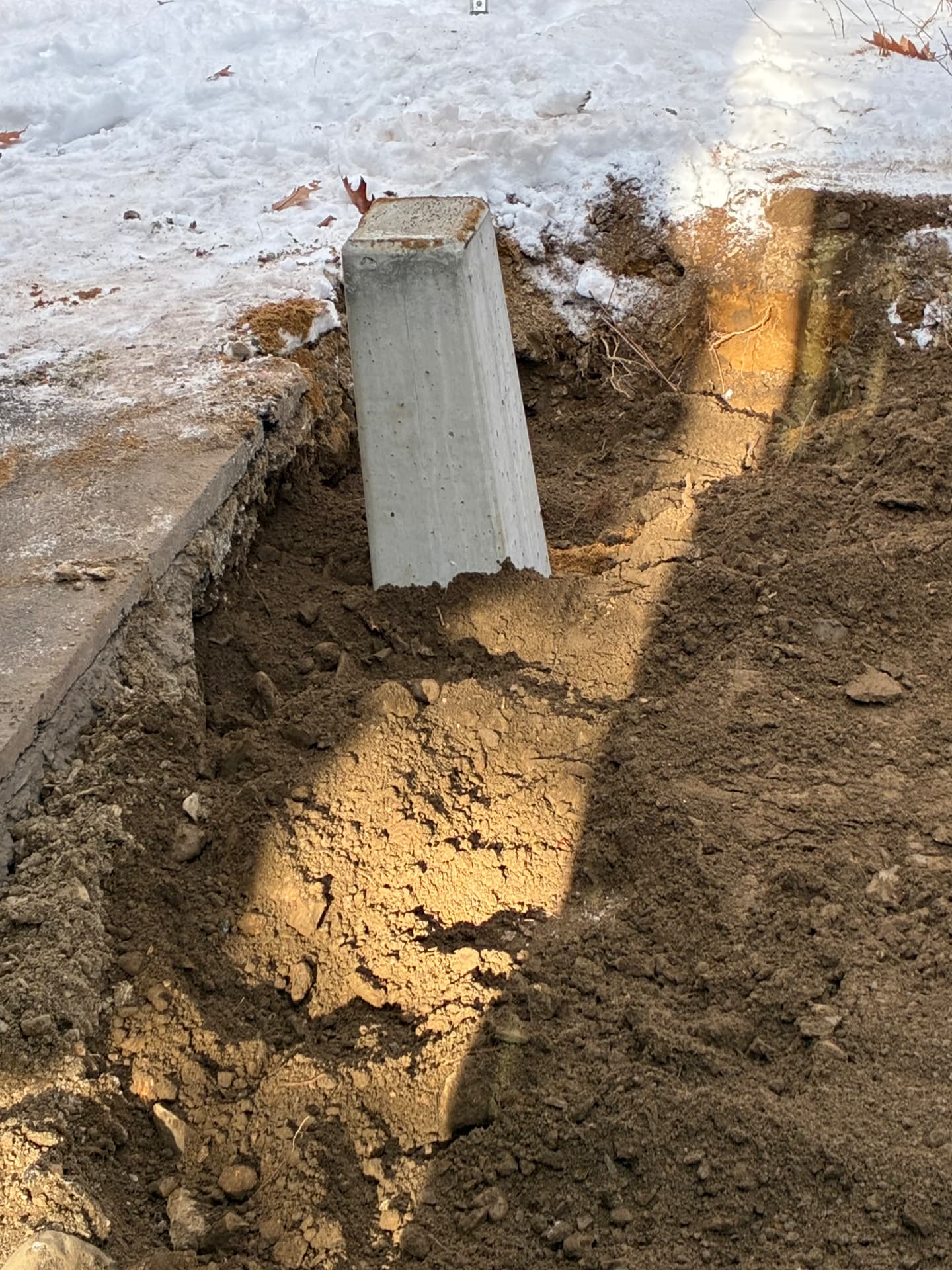 Dug out around an old concrete post base in winter for replacement