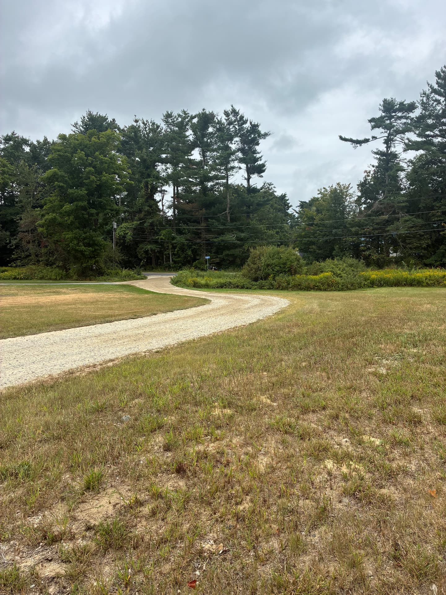Finished gravel driveway curving through an open field in Southern Maine