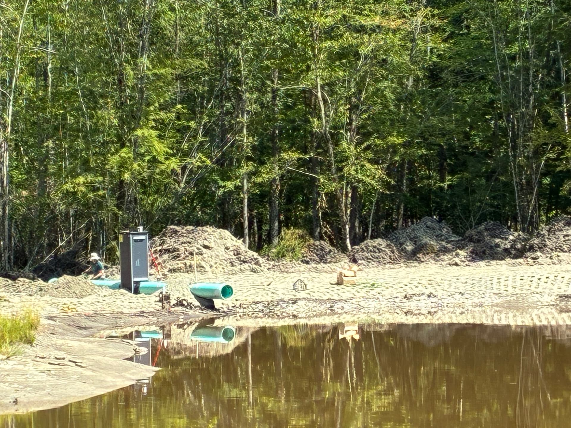 New pond outlet structure and green drainage pipe set into a freshly graded shoreline